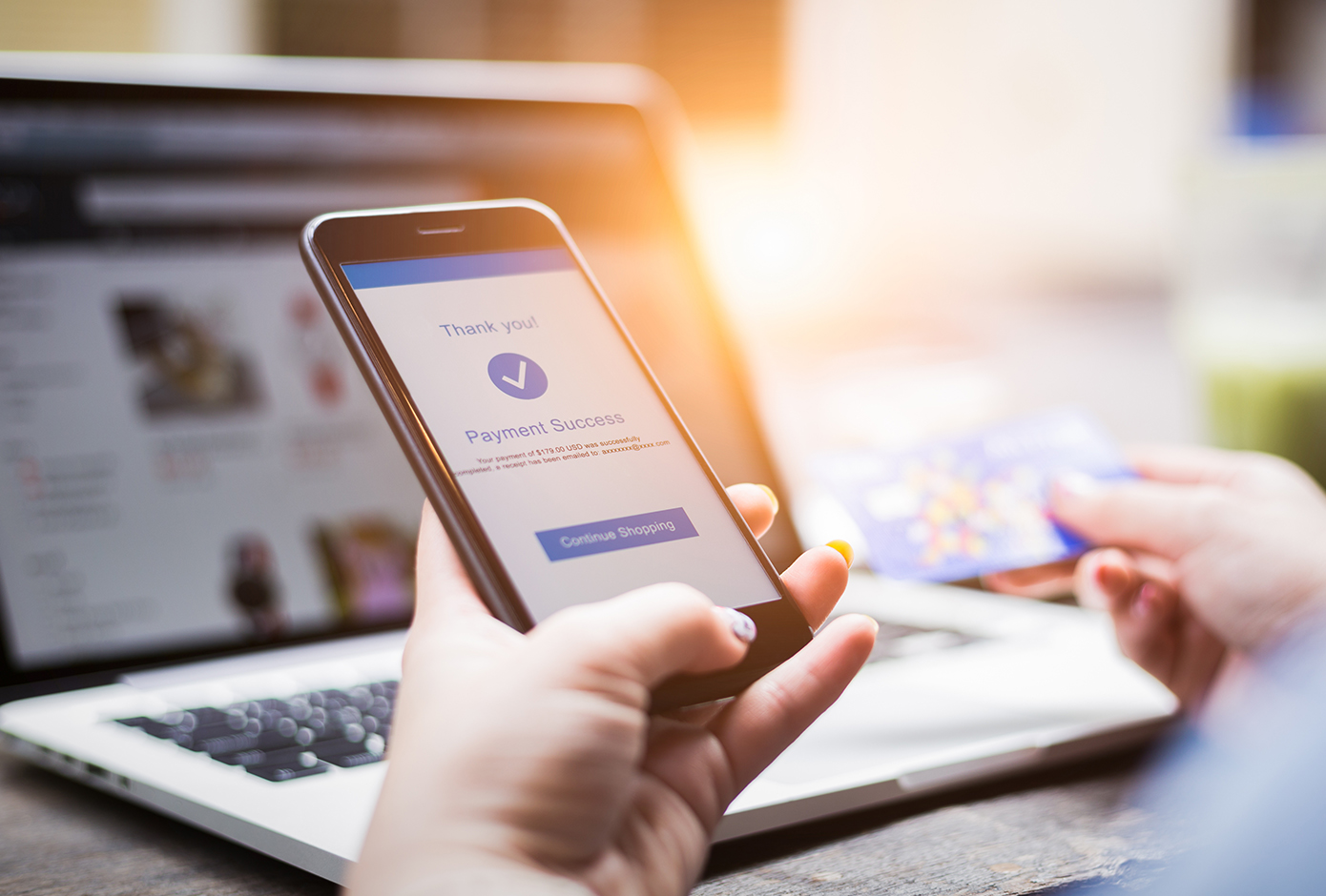 user making payment on mobile phone with laptop in background